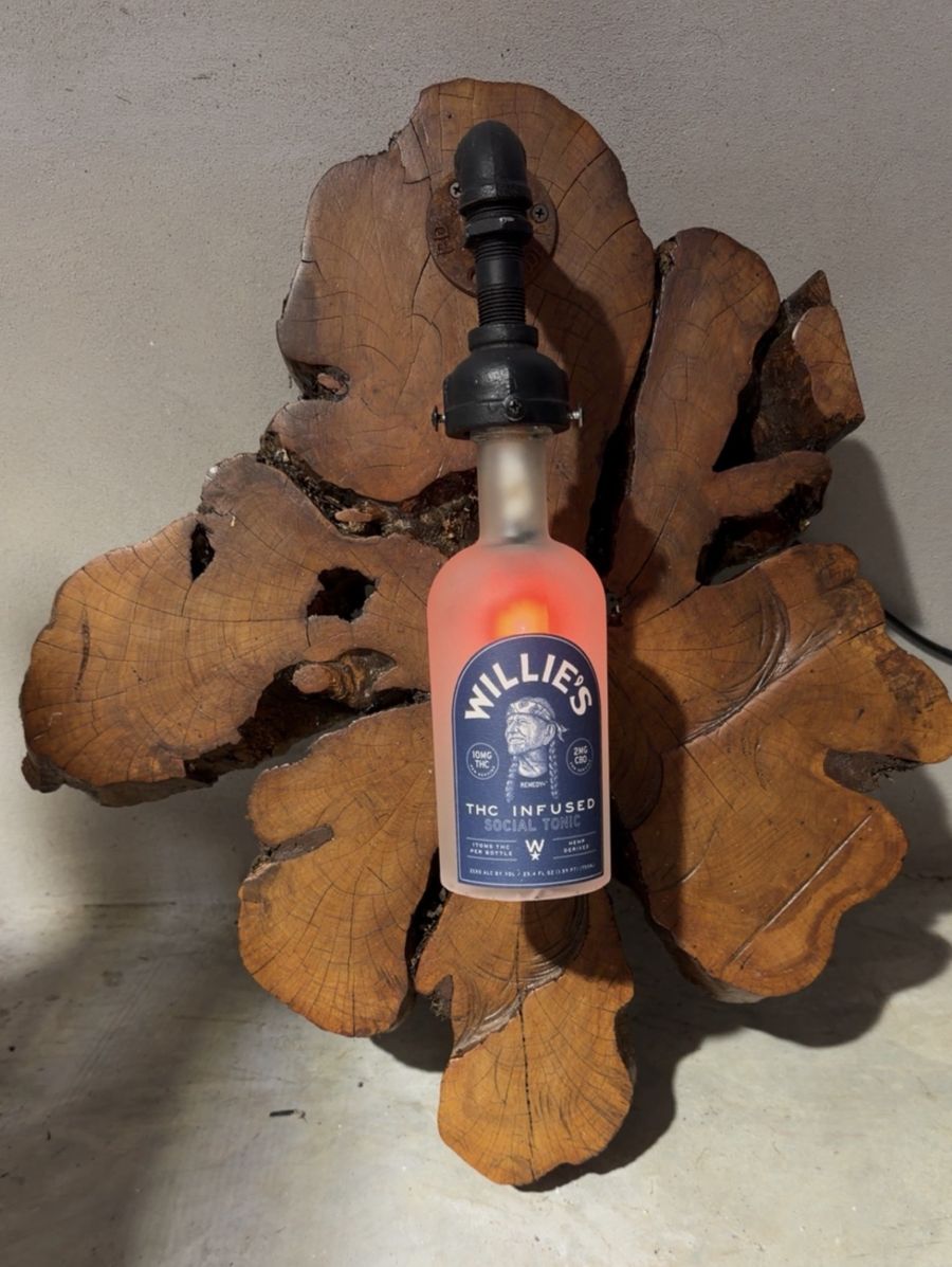 Willie's Bottle Lamp glowing on a natural wood burl slab
